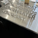 Decorative wall with text 'The Coat, The Sweater, The Shirt' on a reflective surface.