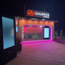Neon sign for 'Olive Churros' at night with a brick wall background