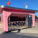 Pink food truck with watermelon design on a paved area under a clear blue sky.