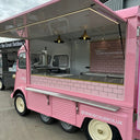 Pink food truck with a brick-patterned design on a cloudy day.