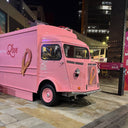 Pink ice cream truck with heart designs on a city street at night.